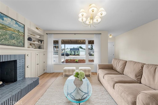 living area featuring light wood finished floors, a fireplace, a chandelier, and built in shelves