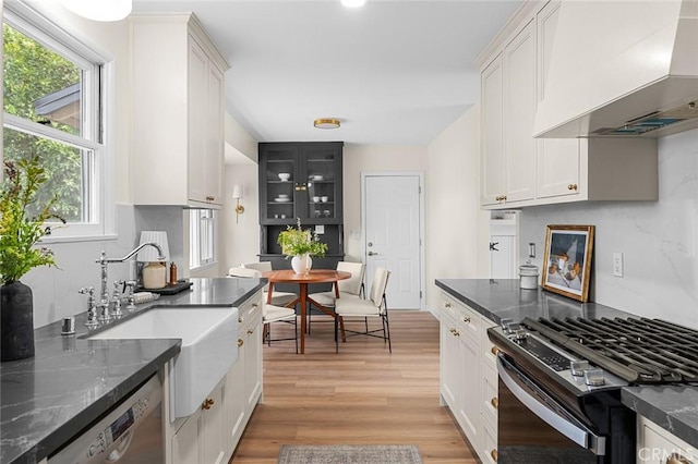 kitchen featuring light wood-style flooring, white cabinetry, stainless steel dishwasher, wall chimney exhaust hood, and gas range