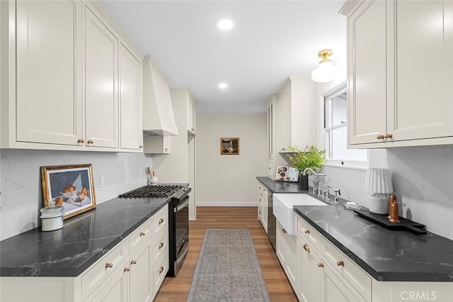 kitchen featuring custom exhaust hood, decorative backsplash, a sink, gas range, and light wood-type flooring