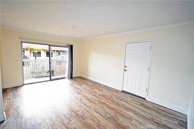 empty room featuring crown molding, baseboards, and wood finished floors