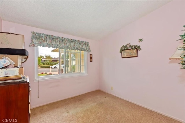 unfurnished room featuring light colored carpet, a textured ceiling, baseboards, and vaulted ceiling