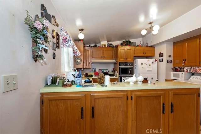 kitchen featuring under cabinet range hood, white appliances, a peninsula, brown cabinetry, and light countertops