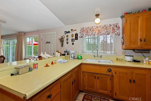 kitchen with a sink, a peninsula, brown cabinetry, and light countertops