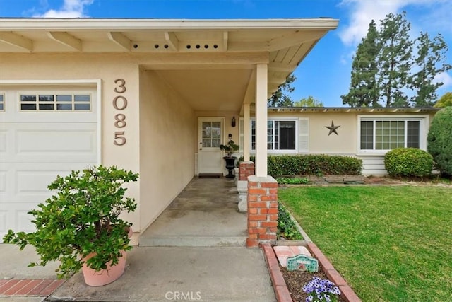 view of exterior entry with a lawn, a garage, and stucco siding