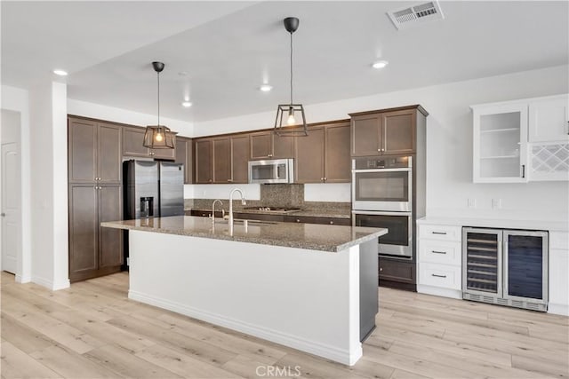 kitchen with wine cooler, stainless steel appliances, visible vents, light wood-style floors, and dark stone countertops