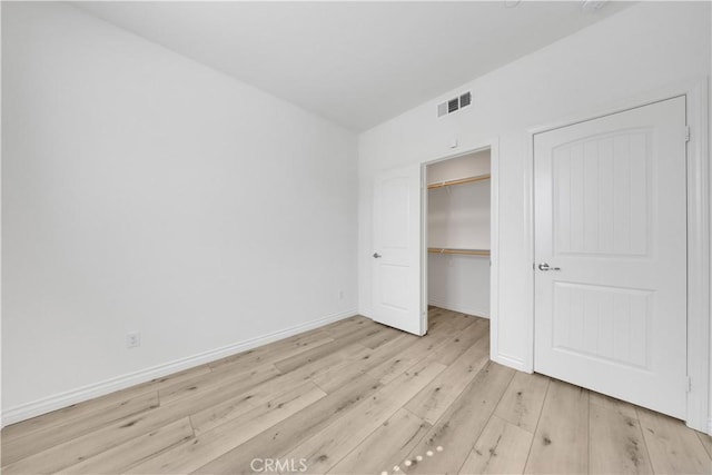 unfurnished bedroom with visible vents, baseboards, light wood-style floors, a closet, and a walk in closet