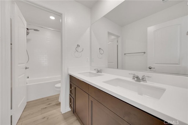 full bathroom with toilet, double vanity, a sink, and wood finished floors