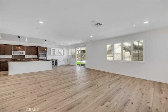 unfurnished living room featuring light wood finished floors, recessed lighting, visible vents, beverage cooler, and baseboards