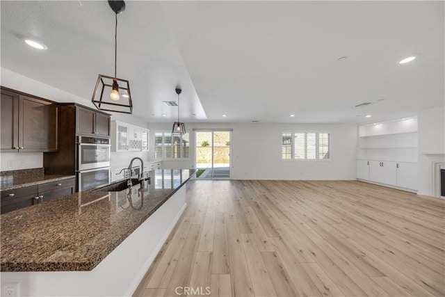 kitchen featuring stainless steel double oven, a sink, open floor plan, dark brown cabinets, and light wood finished floors