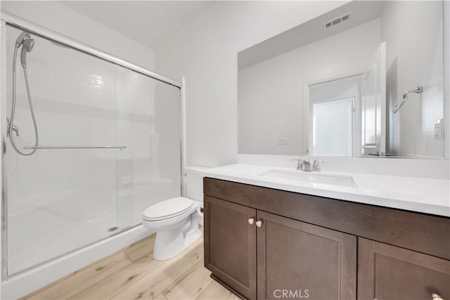 bathroom with visible vents, toilet, a stall shower, vanity, and wood finished floors