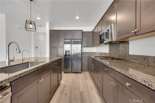 kitchen featuring appliances with stainless steel finishes, a sink, light wood-style flooring, and dark brown cabinetry