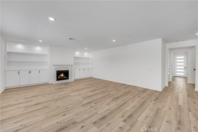 unfurnished living room featuring built in features, recessed lighting, visible vents, light wood-type flooring, and a lit fireplace