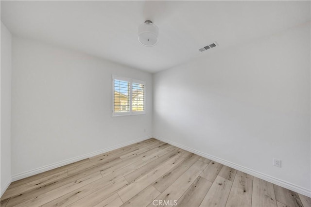 empty room with wood finished floors, visible vents, and baseboards