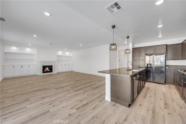 kitchen with dark brown cabinetry, visible vents, a glass covered fireplace, appliances with stainless steel finishes, and dark stone countertops