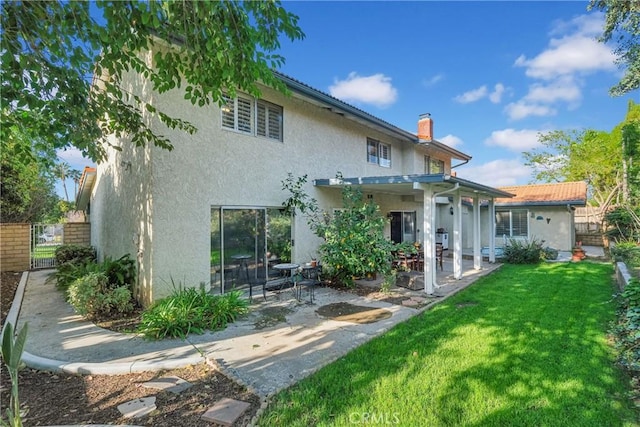 rear view of house with a patio, a chimney, fence, a yard, and stucco siding