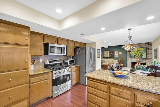 kitchen featuring a fireplace, wood finished floors, appliances with stainless steel finishes, decorative backsplash, and brown cabinets