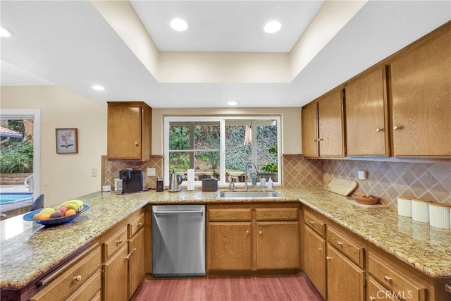 kitchen featuring brown cabinets, a peninsula, a sink, light wood-style floors, and stainless steel dishwasher