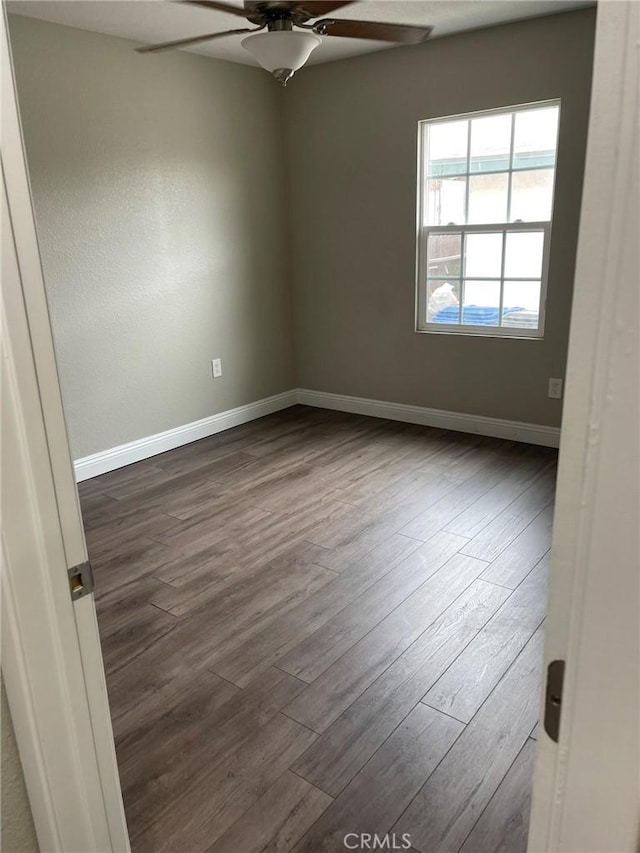 unfurnished room featuring a ceiling fan, dark wood-style flooring, and baseboards