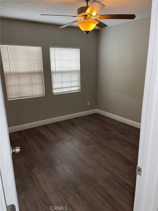 unfurnished room featuring dark wood-style flooring, a ceiling fan, and baseboards