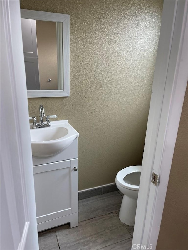 bathroom featuring baseboards, a textured wall, toilet, wood finished floors, and vanity