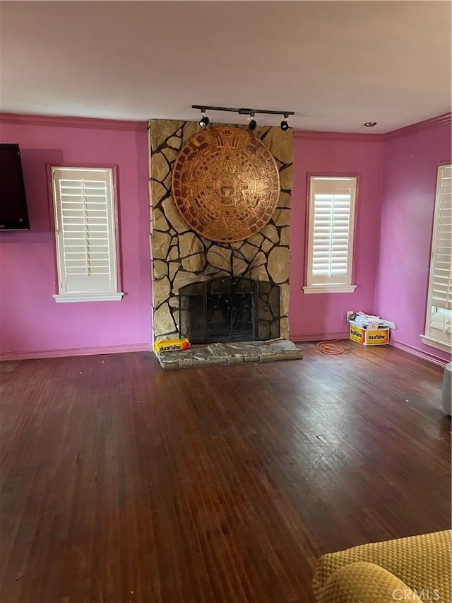 unfurnished living room with crown molding, a stone fireplace, baseboards, and wood finished floors