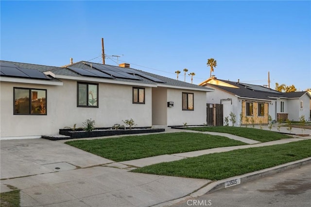 view of front of property featuring stucco siding, roof mounted solar panels, a front yard, and fence