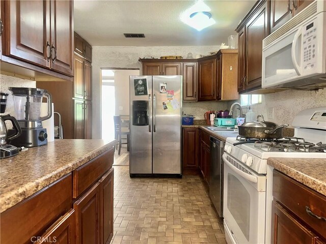 kitchen featuring a sink, brick floor, decorative backsplash, appliances with stainless steel finishes, and visible vents