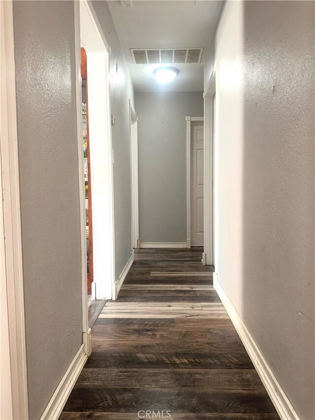 corridor featuring dark wood-type flooring, visible vents, and baseboards