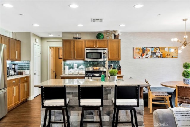 kitchen with stainless steel appliances, a breakfast bar area, dark wood-style floors, and brown cabinetry