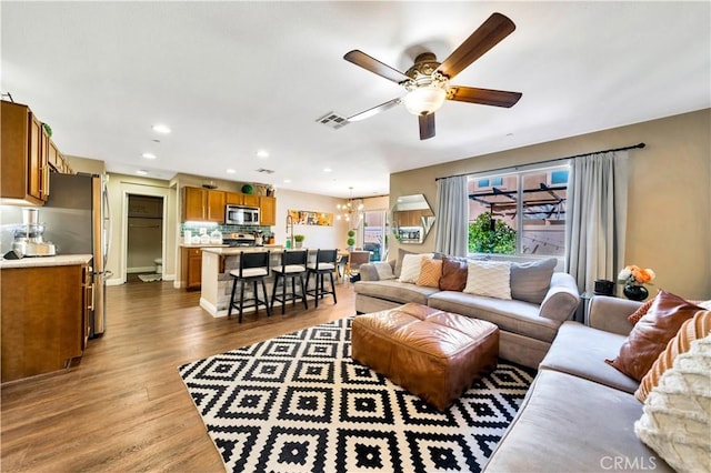 living area featuring recessed lighting, ceiling fan with notable chandelier, visible vents, and dark wood-style flooring