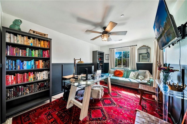 office area with a wainscoted wall, a ceiling fan, and visible vents