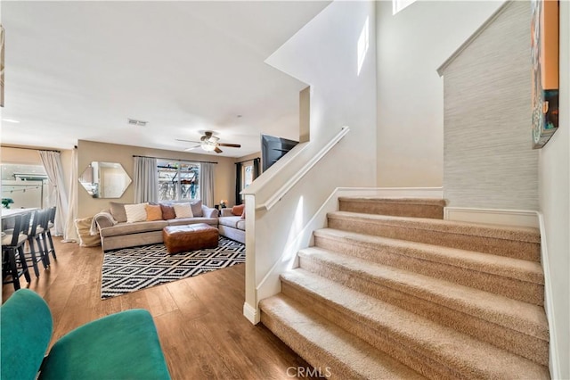 living area with stairway, a ceiling fan, visible vents, and wood finished floors