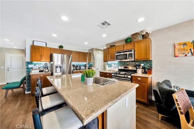 kitchen featuring visible vents, dark wood-style flooring, a sink, stainless steel appliances, and brown cabinets