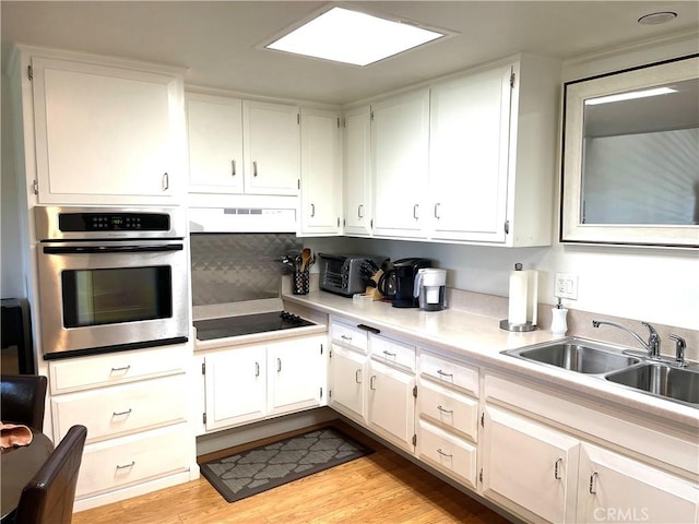 kitchen with light wood-style flooring, a sink, under cabinet range hood, stainless steel oven, and black electric stovetop