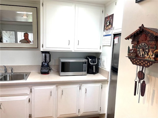 kitchen with white cabinets, stainless steel appliances, light countertops, and a sink