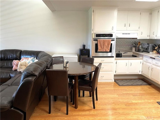 kitchen featuring light wood-style flooring, under cabinet range hood, stainless steel oven, black electric cooktop, and open floor plan