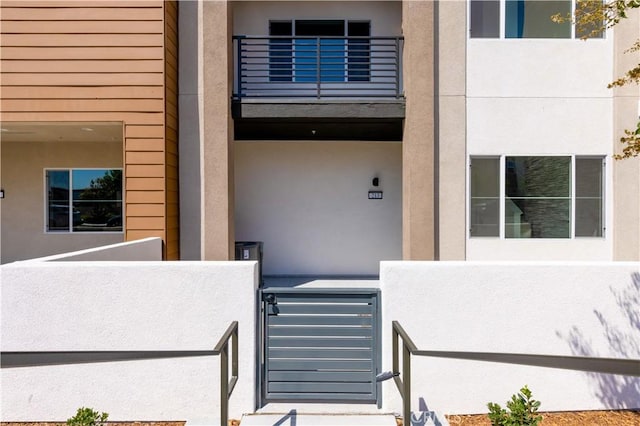 property entrance featuring a balcony, fence, and stucco siding