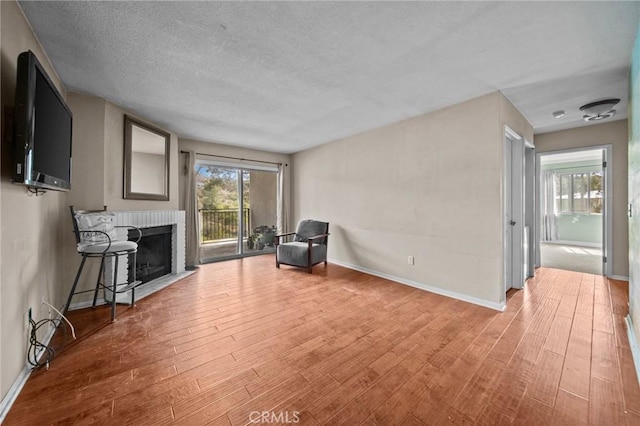 living area featuring a textured ceiling, a brick fireplace, wood finished floors, and baseboards