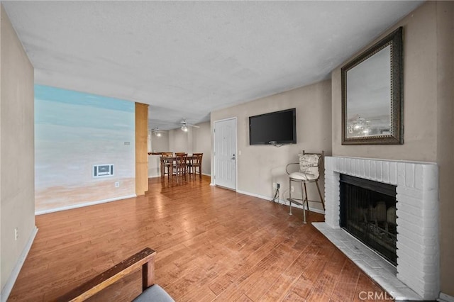 living room with a ceiling fan, a fireplace, baseboards, and wood finished floors