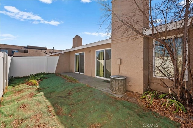 rear view of house featuring a patio, fence, a yard, stucco siding, and a chimney