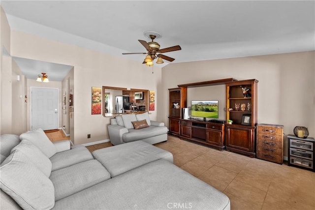 living room with ceiling fan, vaulted ceiling, baseboards, and light tile patterned floors