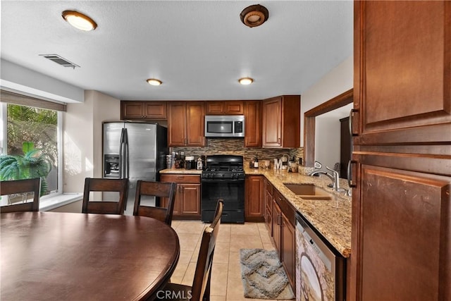 kitchen featuring light tile patterned floors, decorative backsplash, light stone counters, appliances with stainless steel finishes, and a sink