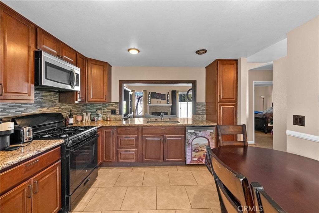 44680 La Paz Rd, Temecula, CA 92592 - kitchen featuring black range with gas stovetop, light stone counters, a sink, stainless steel microwave, and backsplash