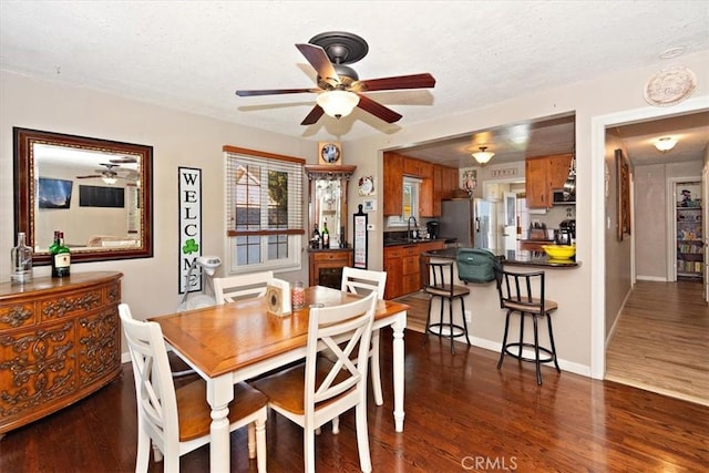 dining area with dark wood-type flooring, a textured ceiling, baseboards, and a ceiling fan