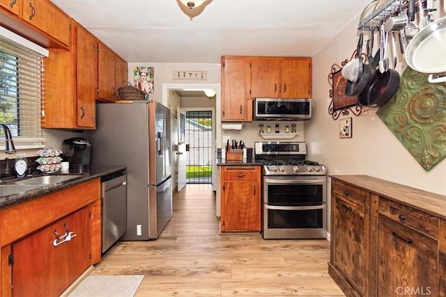 kitchen featuring appliances with stainless steel finishes, brown cabinets, a sink, and light wood-style flooring