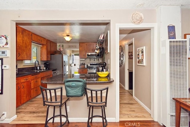 kitchen with a heating unit, dark countertops, stainless steel appliances, light wood-style floors, and a sink