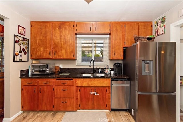 kitchen with light wood finished floors, a toaster, brown cabinets, stainless steel appliances, and a sink