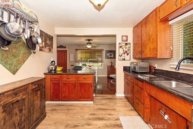 kitchen with light wood finished floors, a toaster, dark stone counters, ceiling fan, and a sink