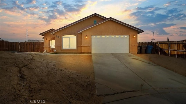 view of front of property with concrete driveway, an attached garage, fence, and stucco siding