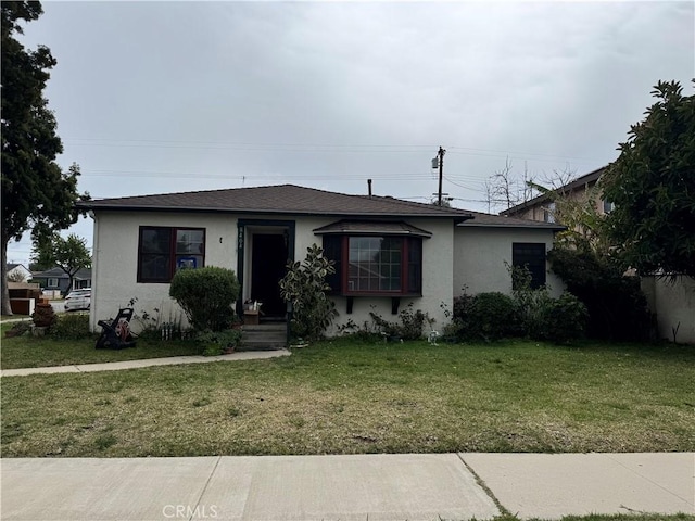 view of front of property with roof with shingles, a front yard, and stucco siding